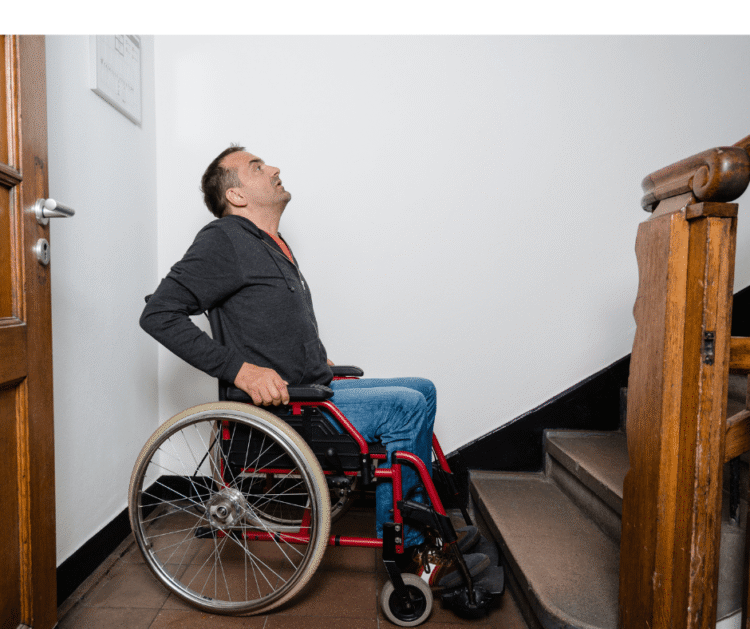 A person in a wheelchair is at the base of a staircase, looking up..