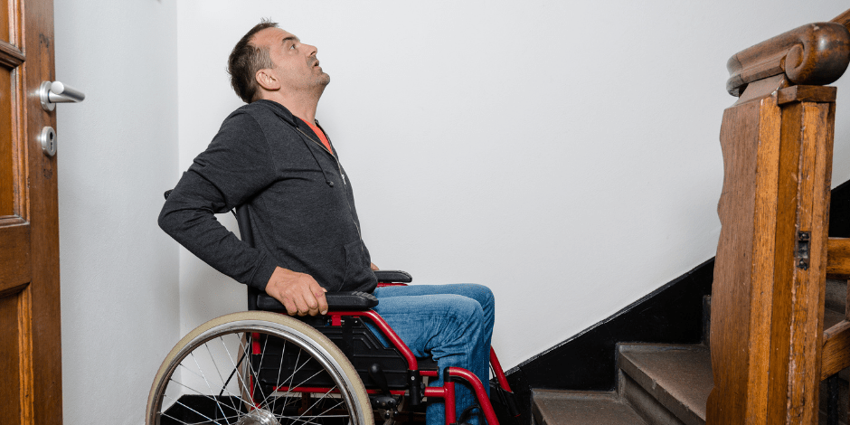 A person in a wheelchair is at the base of a staircase, looking up..